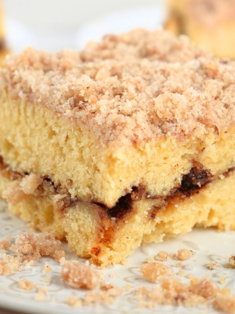 A close up of a slice of sourdough discard coffee cake on a decorative plate with crumble topping scattered in the foreground