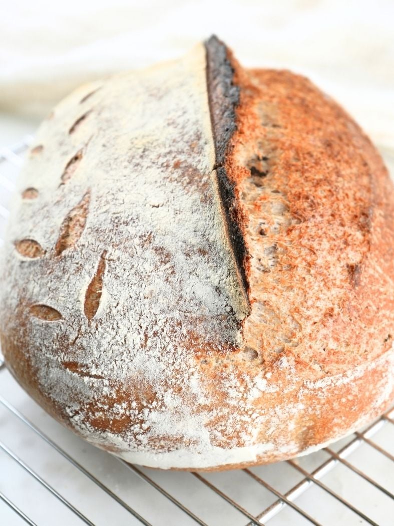 A boule of sourdough bread on a wire cooling rack