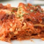 Close up of a slice of slow cooker lasagna on a white plate, shown with herb garnish
