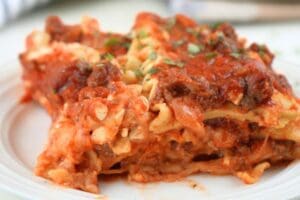 Close up of a slice of slow cooker lasagna on a white plate, shown with herb garnish