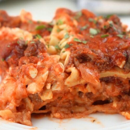 Close up of a slice of slow cooker lasagna on a white plate, shown with herb garnish