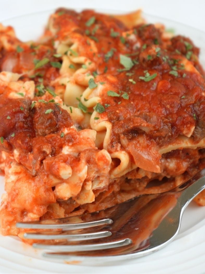 Close up of slow cooker lasagna on a white plate with a fork in the foreground