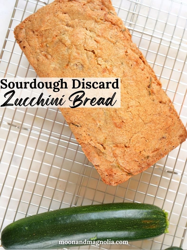 A loaf of sourdough discard zucchini bread on a wire rack with a fresh zucchini