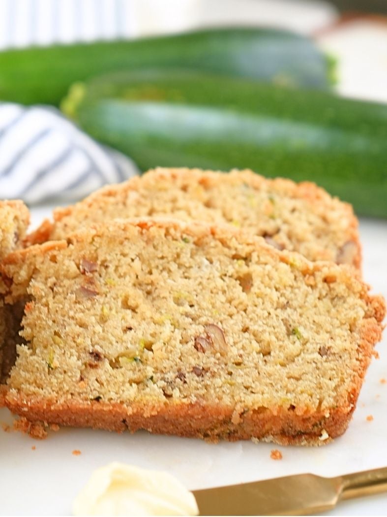 Slices of sourdough discard zucchini bread with a buttered knife the foreground