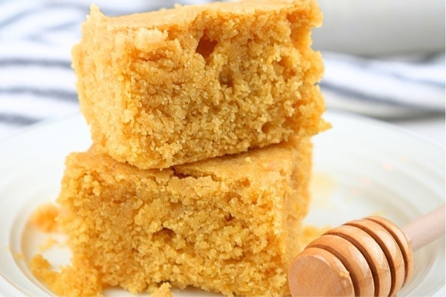 Two slices of cornbread made with fresh milled flour next to a honey dipper