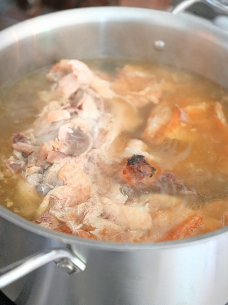 Chicken bones and water boiling in a stainless steel stock pot