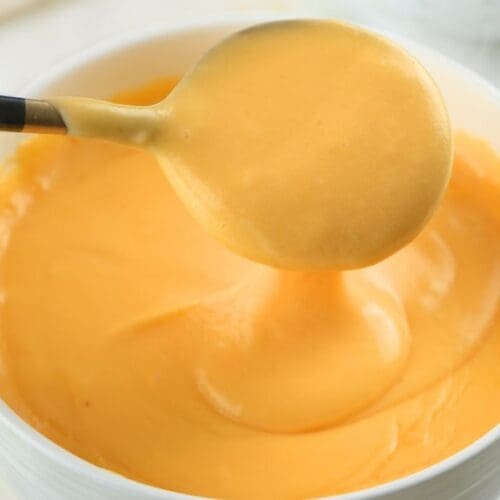 A close up of a spoon lifting sourdough discard cheese sauce out of a bowl