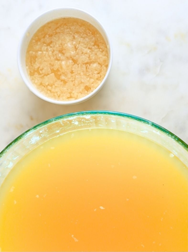 Chicken broth in a large bowl and the skimmed fat in a small white bowl