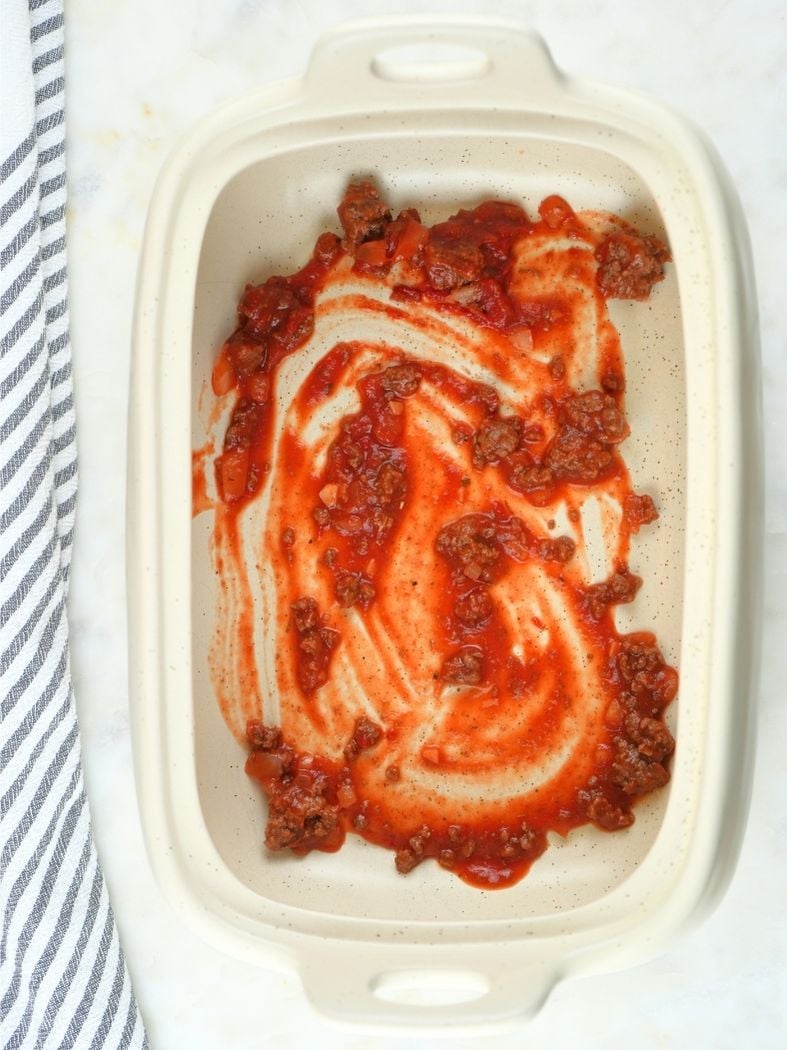 A baking dish with a thin layer of sauce on the bottom