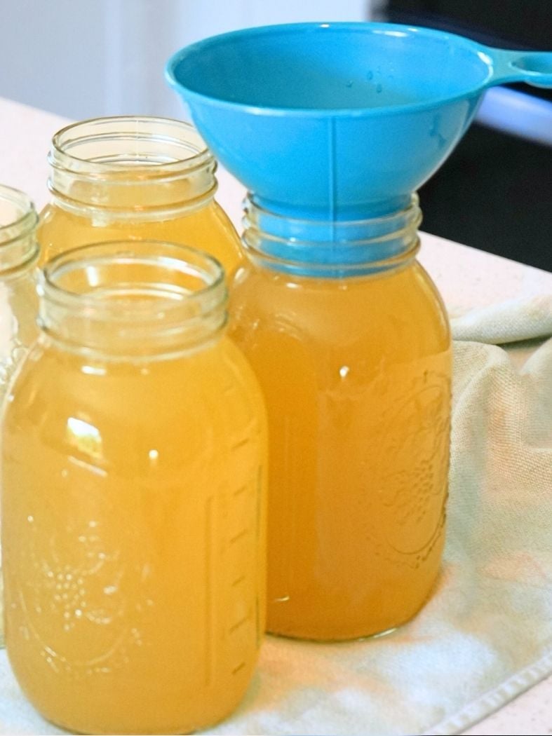 Mason jars filled with chicken broth, one jar with a canning funnel on top