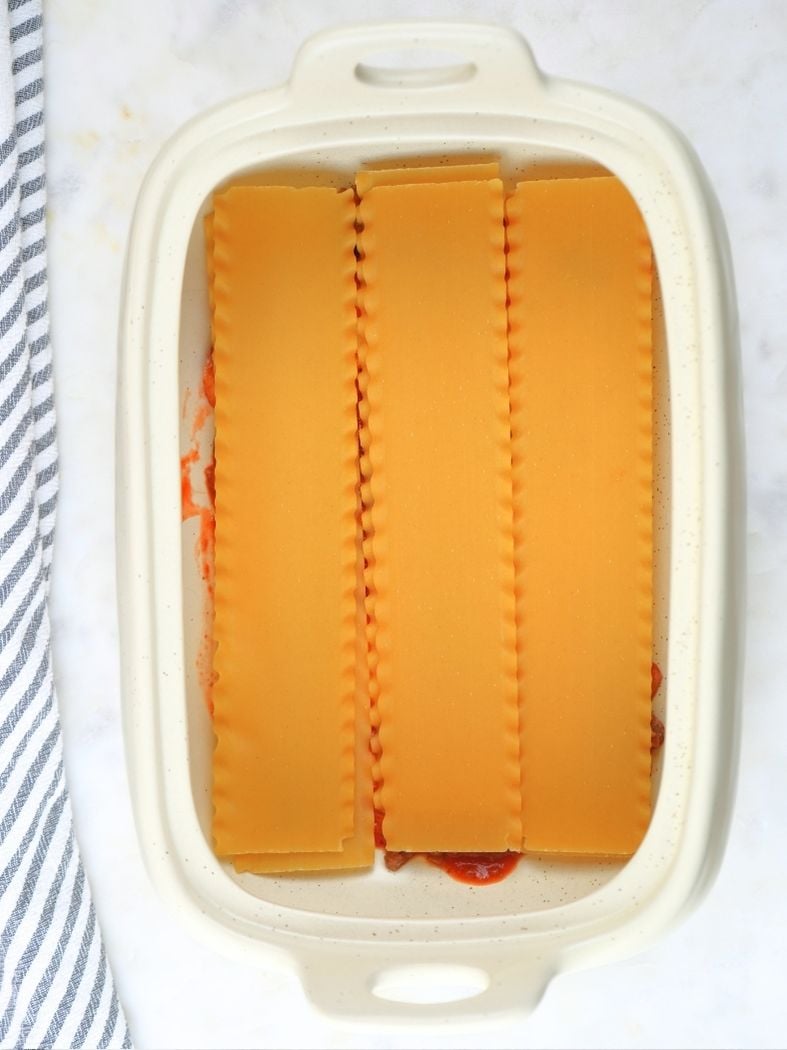 A baking dish with uncooked noodles layered in the bottom
