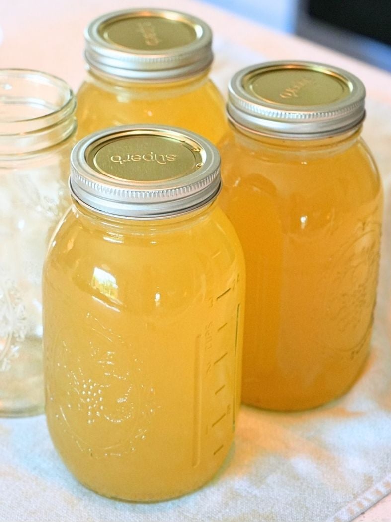 Jars filled with chicken broth with canning lids and rings, showing how to can chicken broth