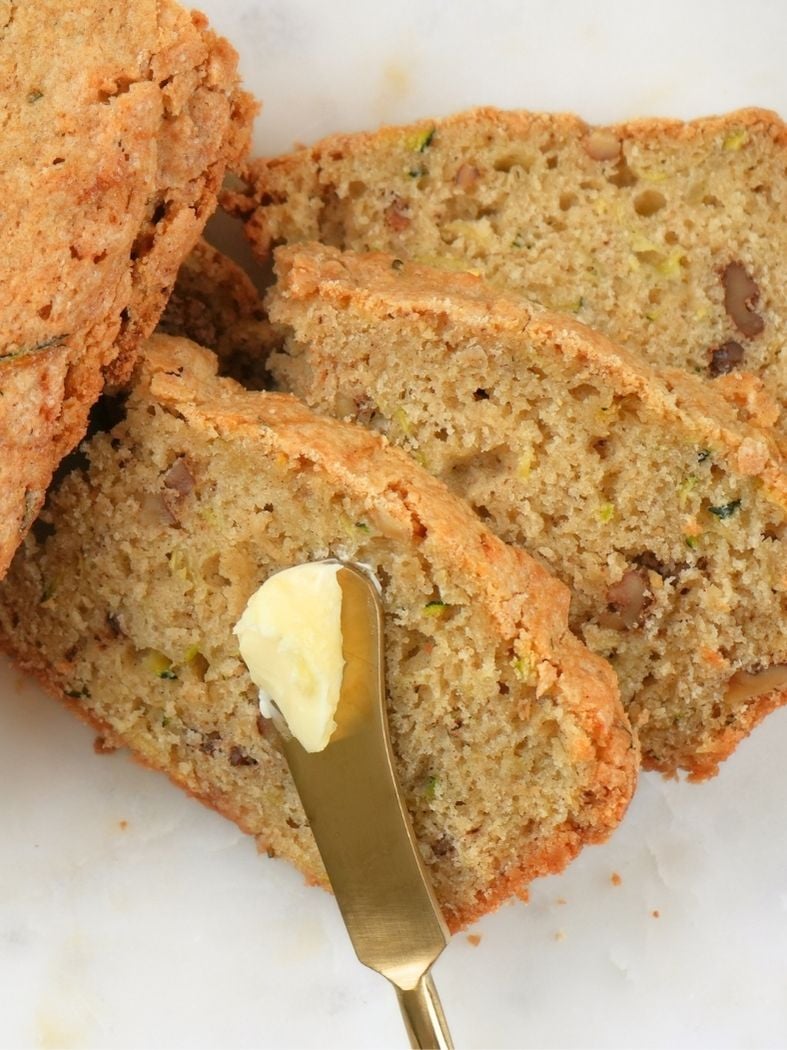 Stacked sliced of sourdough zucchini bread with a buttered knife