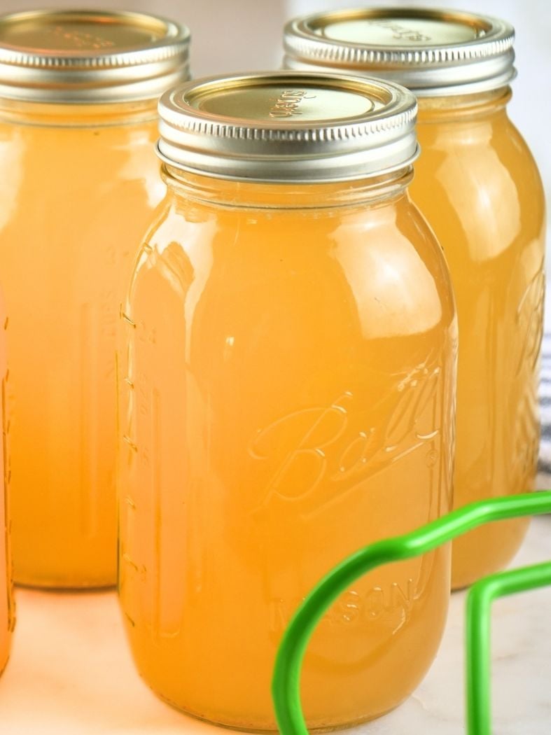 Jars of home-canned chicken broth and canning tongs in the foreground
