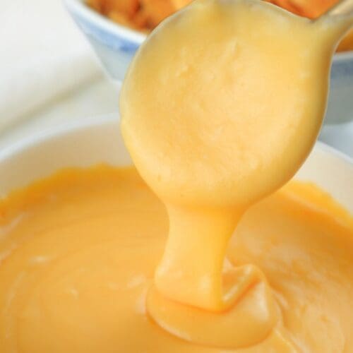 A spoon lifting sourdough discard cheese sauce out of a bowl.
