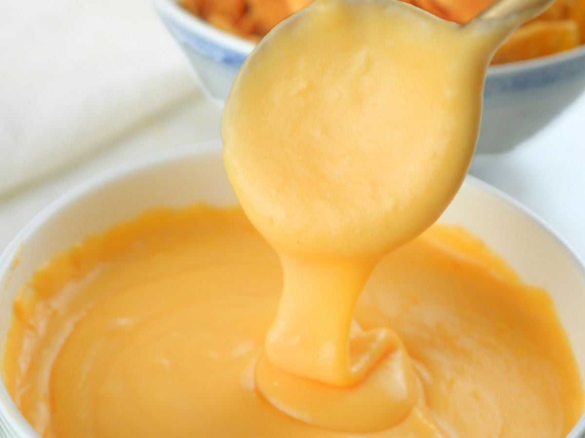 A spoon lifting sourdough discard cheese sauce out of a bowl.