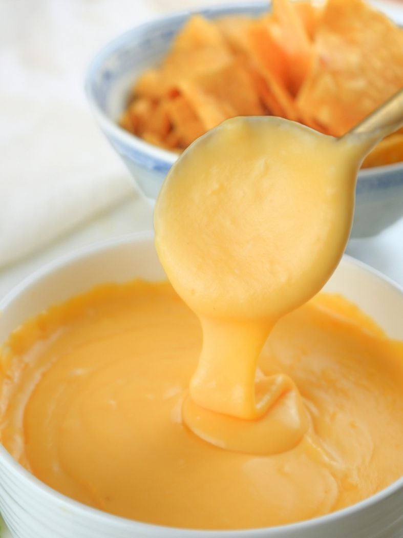 A spoon lifting sourdough discard cheese sauce out of a bowl