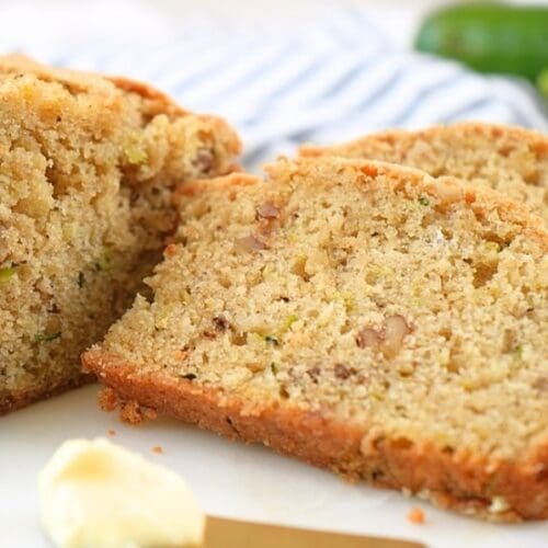 A sliced loaf of sourdough discard zucchini bread with butter in the foreground