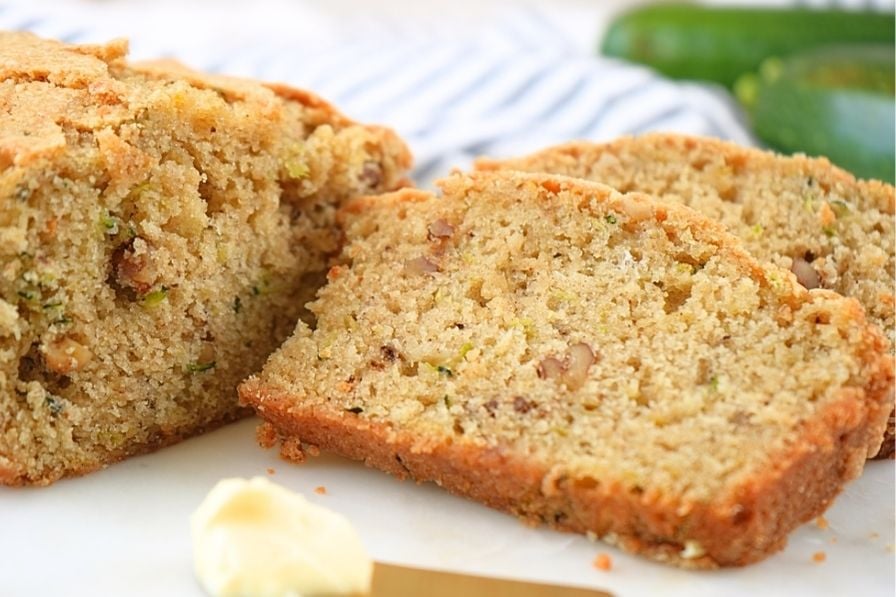 A sliced loaf of sourdough discard zucchini bread with butter in the foreground
