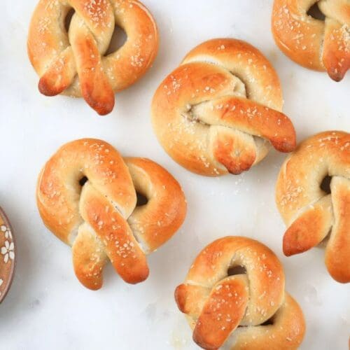 Sourdough soft pretzels scattered on a counter next to a bowls of salt and mustard