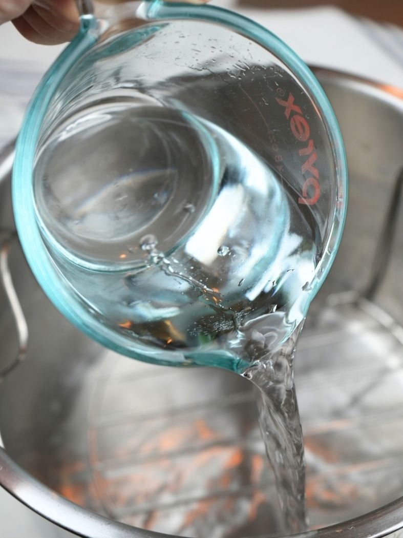A measuring cup of water with the water pouring into an Instant Pot