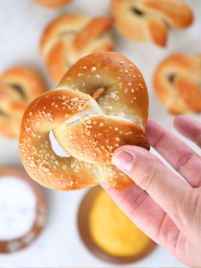 An overhead view of a hand holding a sourdough soft pretzel with more pretzels in the background