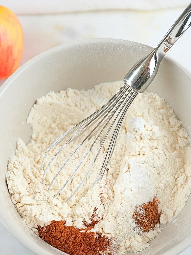 A mixing bowl with dry ingredients and a whisk in it