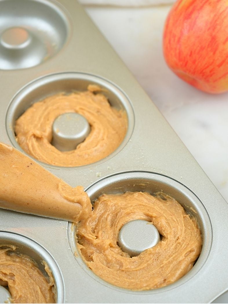 A donut pan filled with batter, shown with a filled piping bag