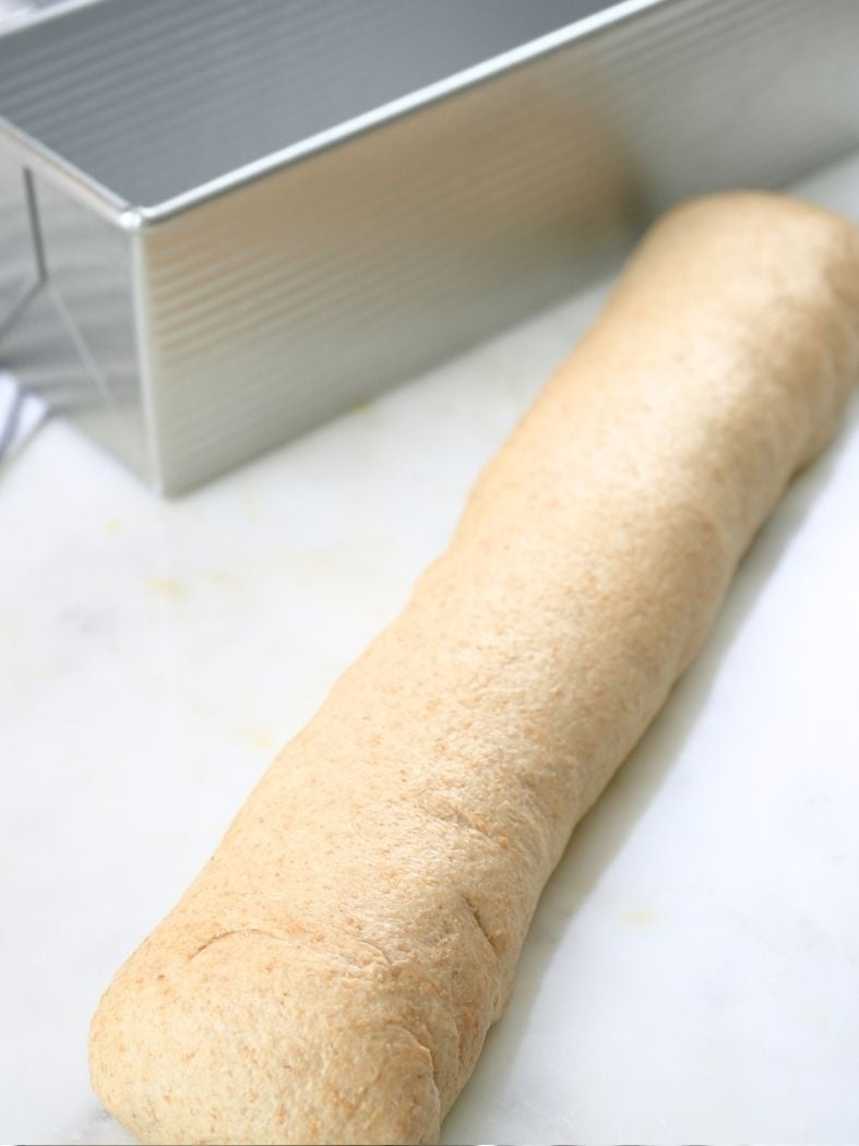 Dough rolled into a log with a Pullman pan in the background