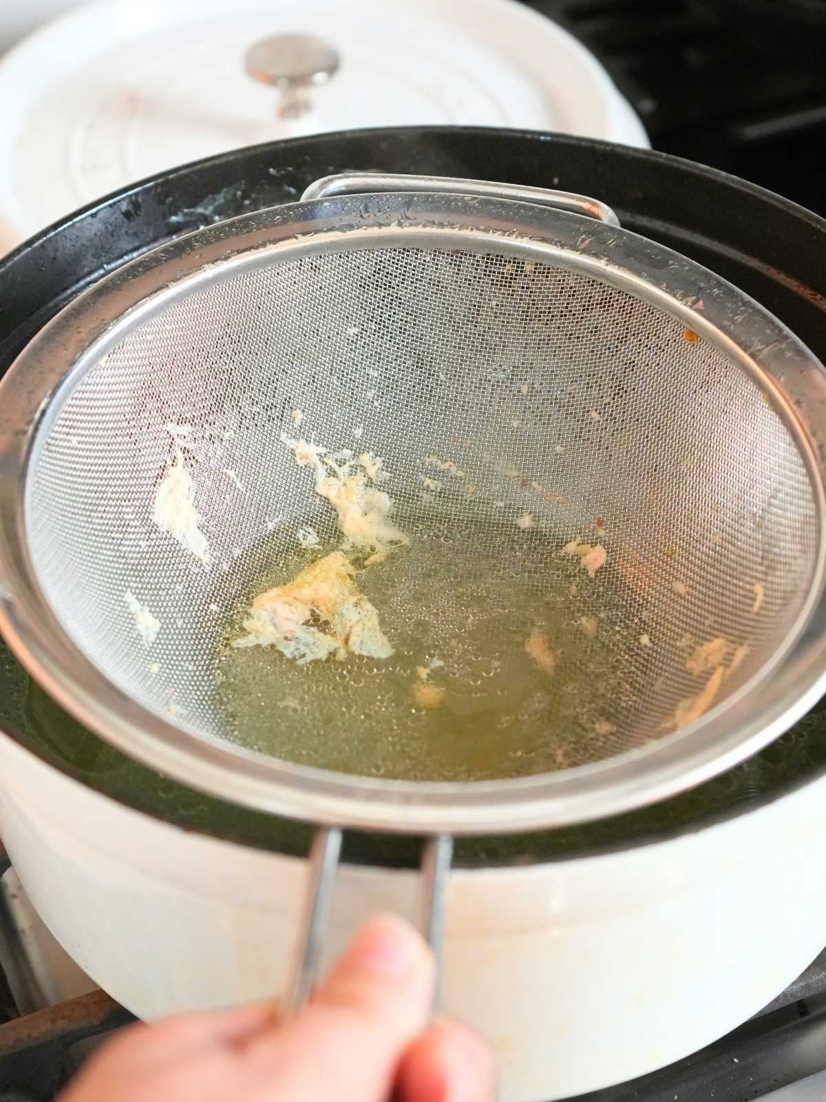 A pot of chicken broth with a fine mesh strainer catching remnants.