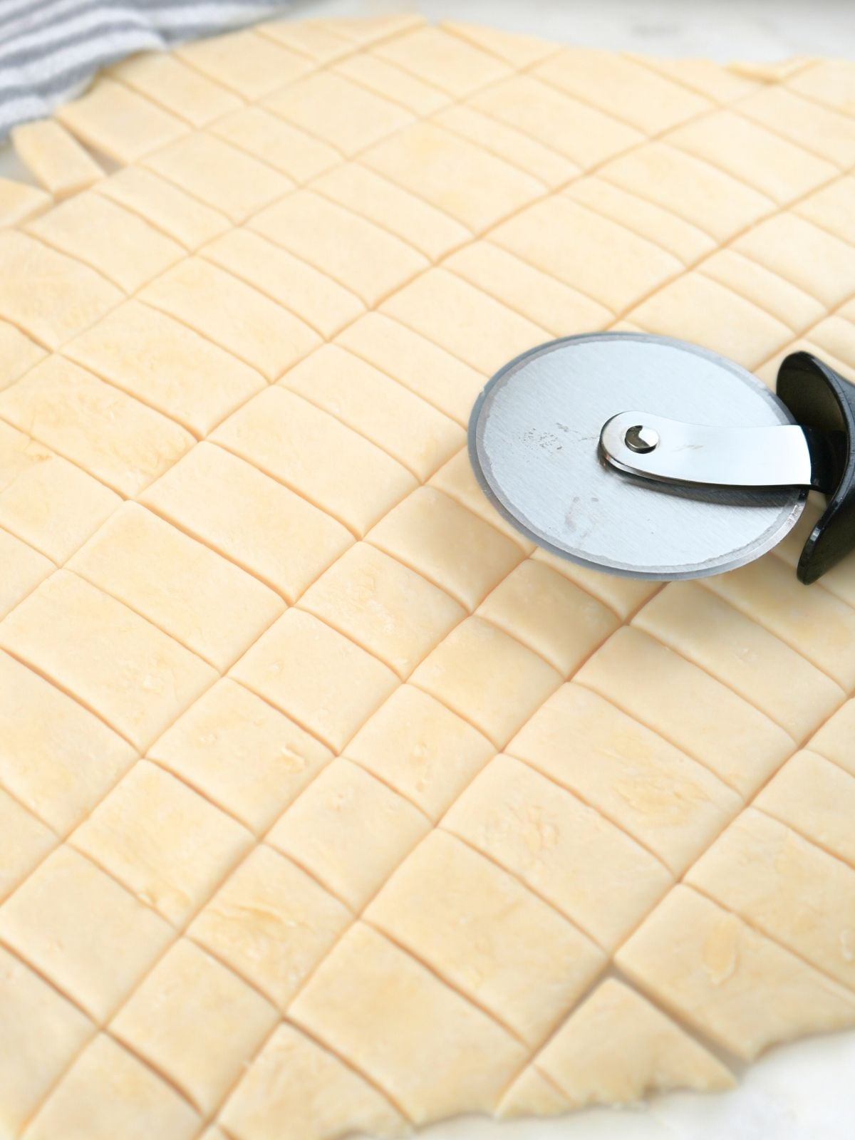 Pastry dough cut into strips, shown with a pizza cutter.