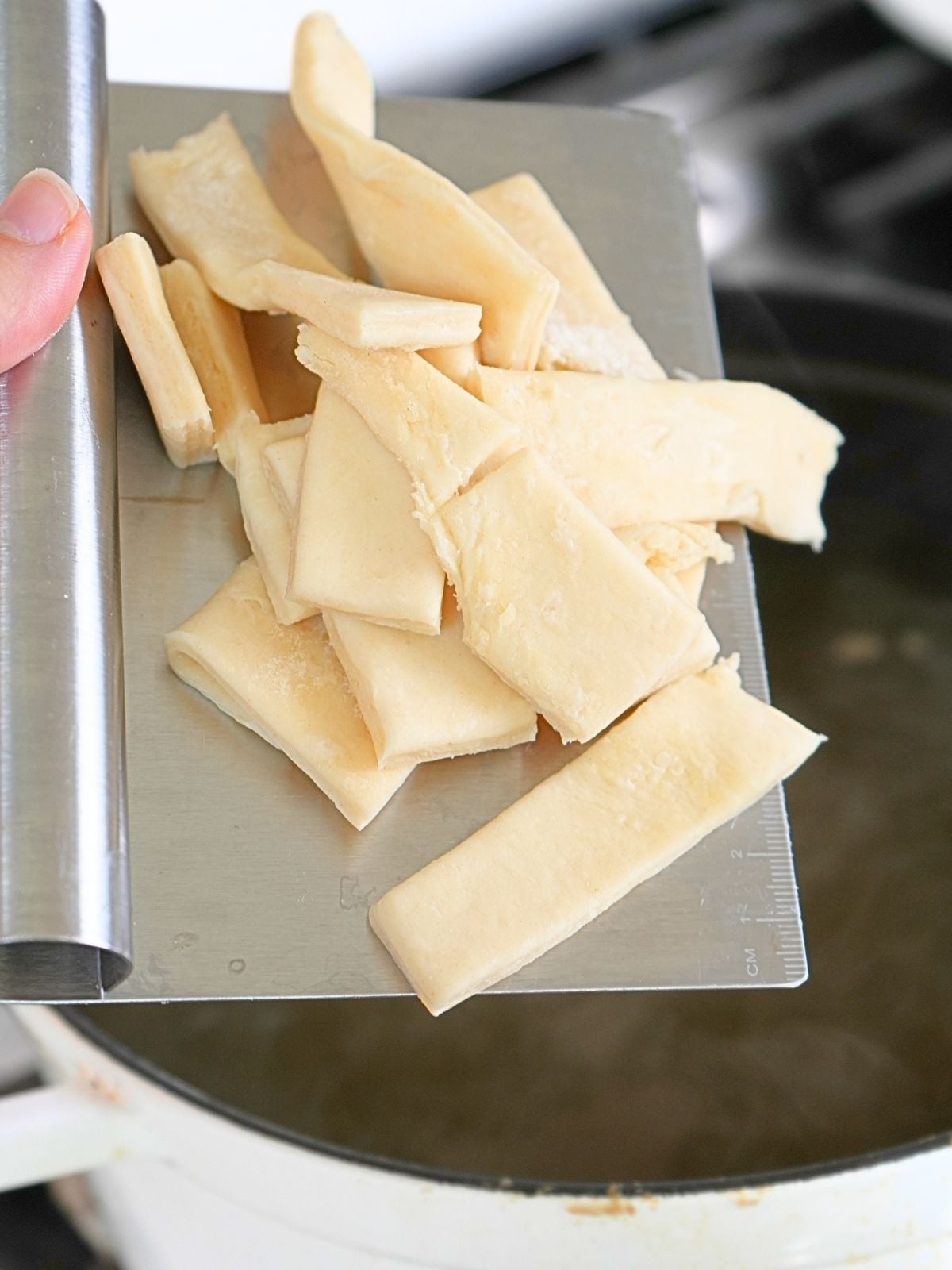 Pastry dough on a bench scraping over a pot of boiling broth.
