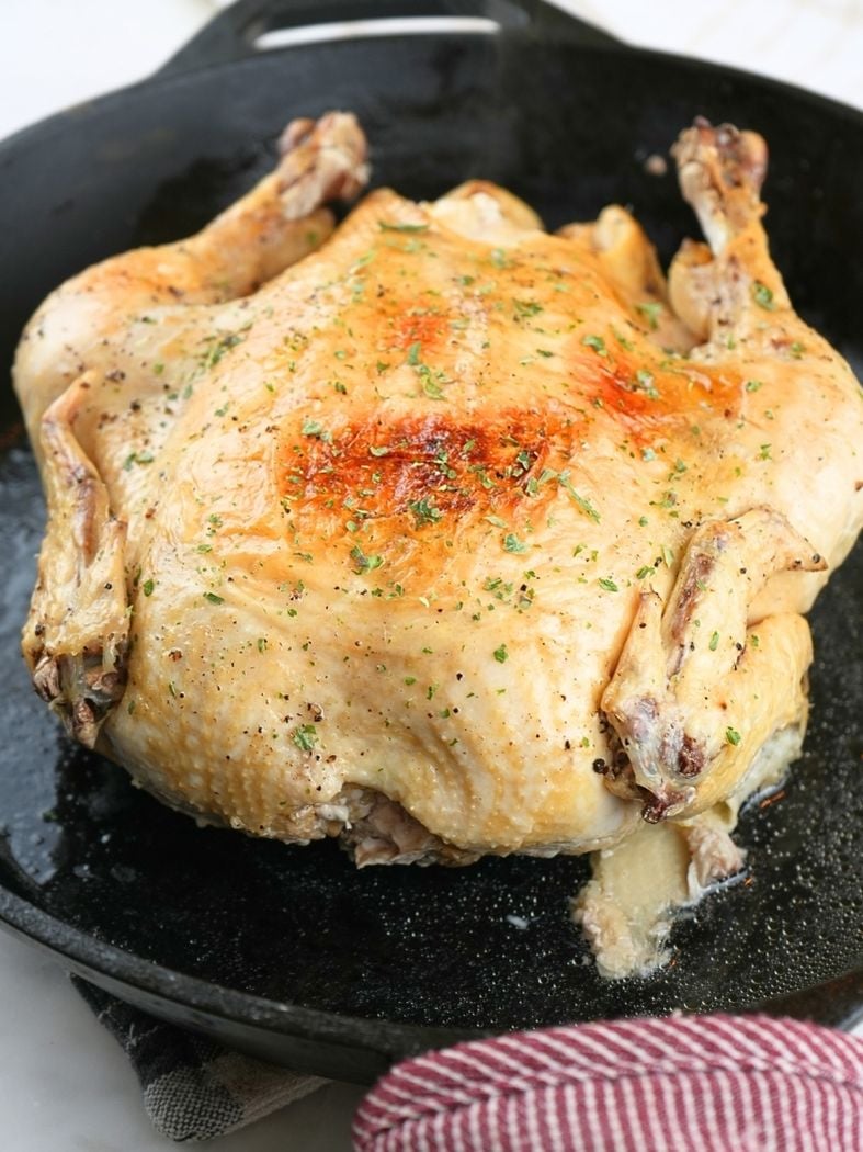 A whole chicken with browned skin in a cast iron skillet
