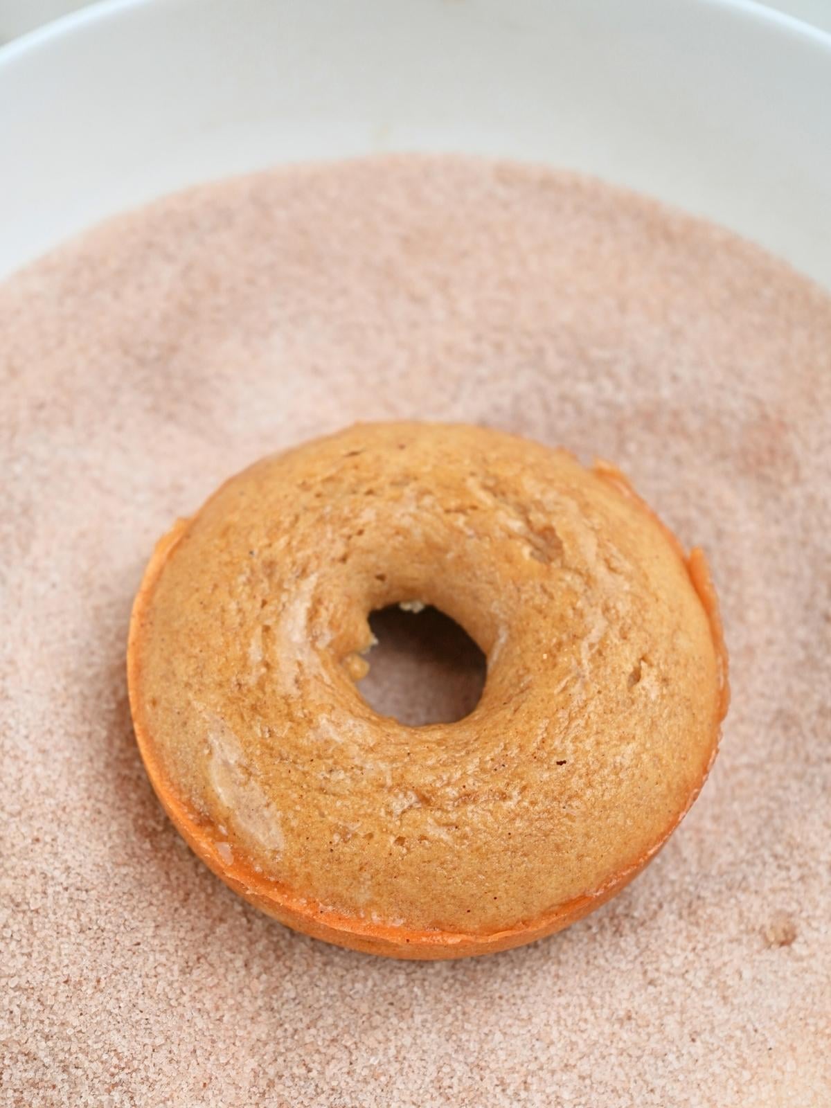 A buttered donut in a dish of cinnamon and sugar.