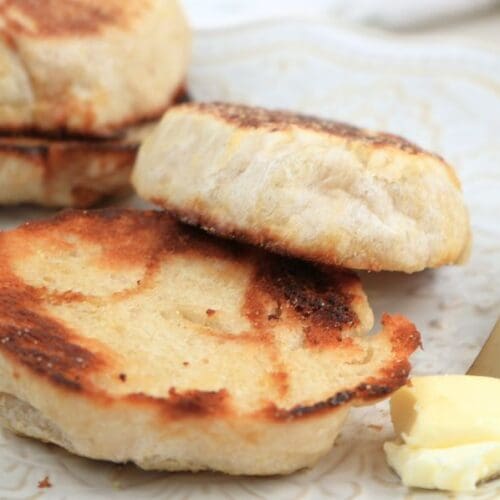 A toasted English muffin on a decorative plate next to a gold knife with butter