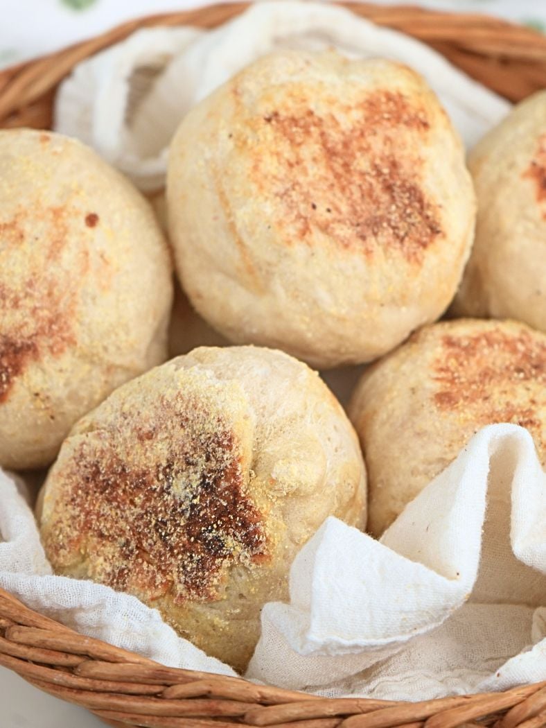 A towel-lined basket filled with sourdough English muffins