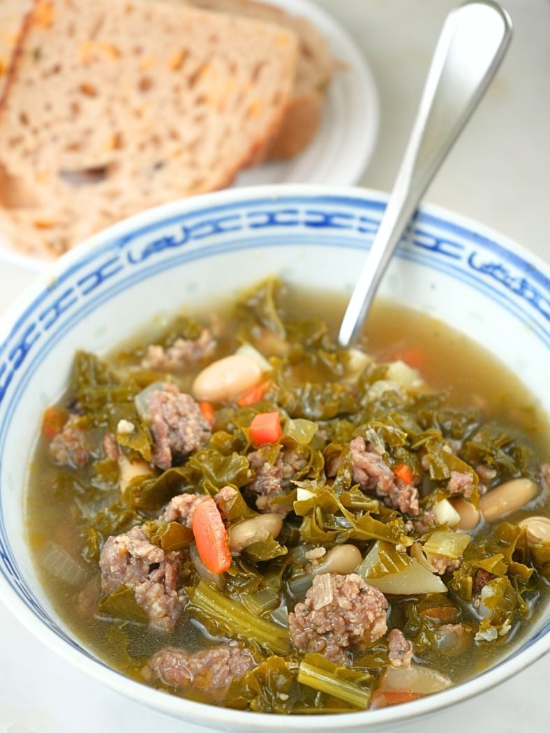 A bowl of sausage, kale, and white bean soup and sourdough bread in the background