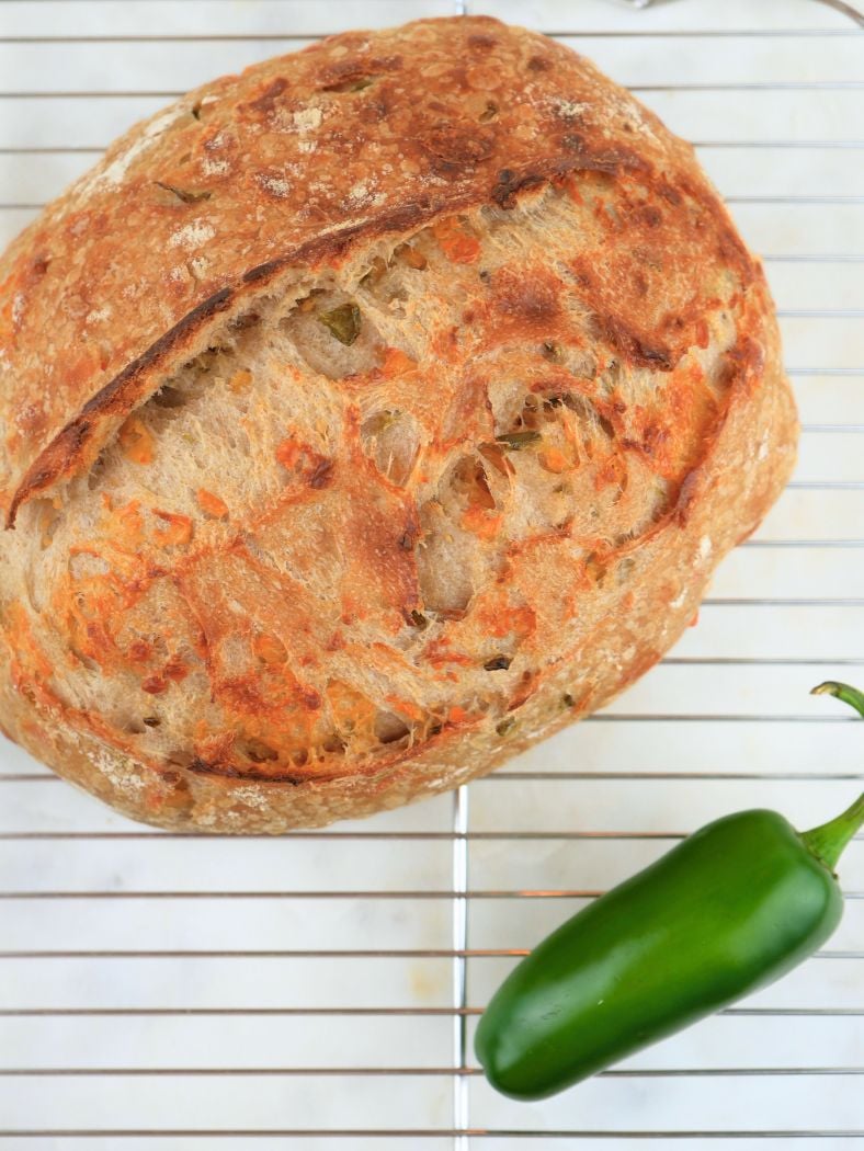 Finished sourdough cheddar jalapeño bread cooling on a wire rack, show next to a fresh jalapeño