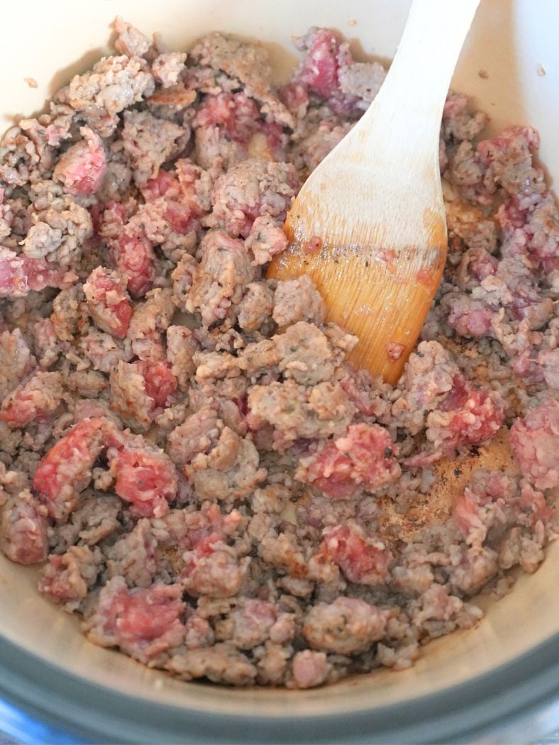 Sweet Italian sausage browning in a Dutch oven, shown with wooden spatula