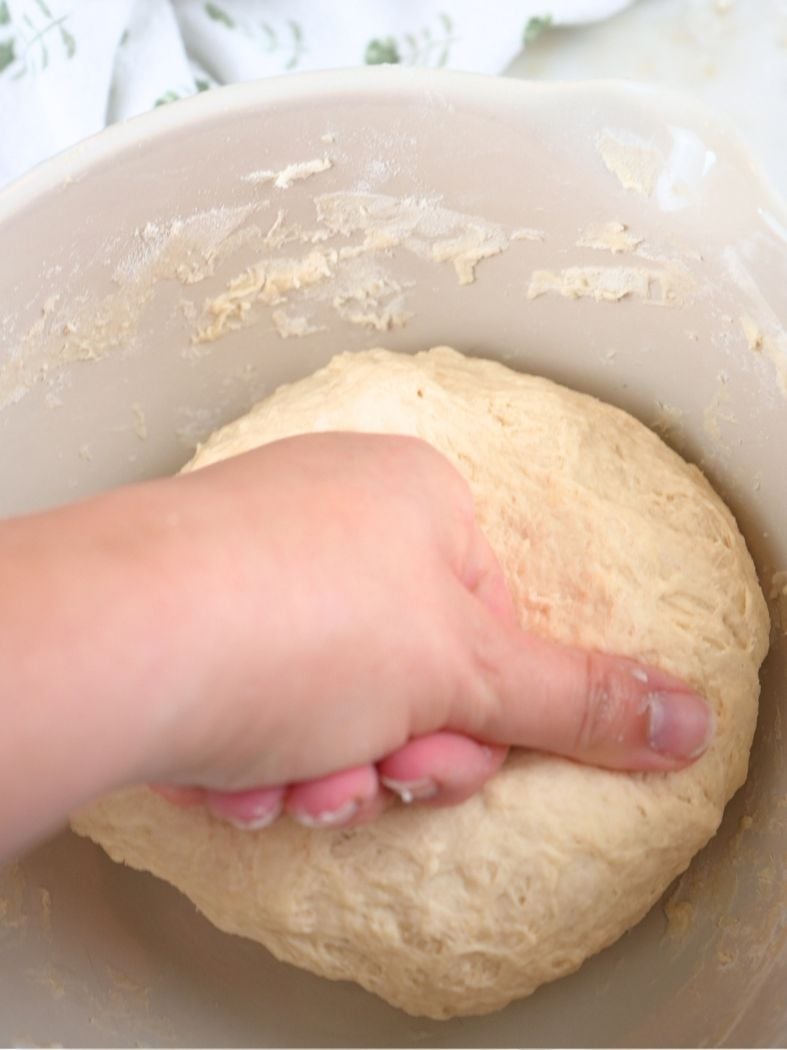 A hand kneading dough in a mixing bowl
