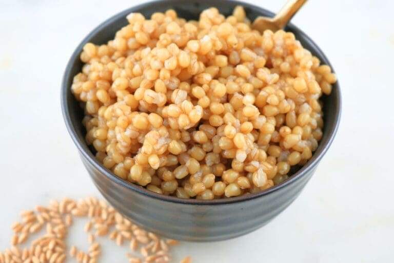 Slow cooker wheat beries in a small black bowl with a gold spoon, shown with dry berries scattered