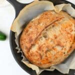 Overhead view of sourdough cheddar jalapeño bread in a Dutch oven, next to a fresh pepper