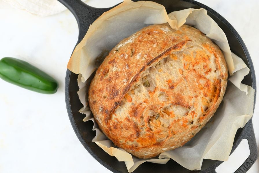 Overhead view of sourdough cheddar jalapeño bread in a Dutch oven, next to a fresh pepper