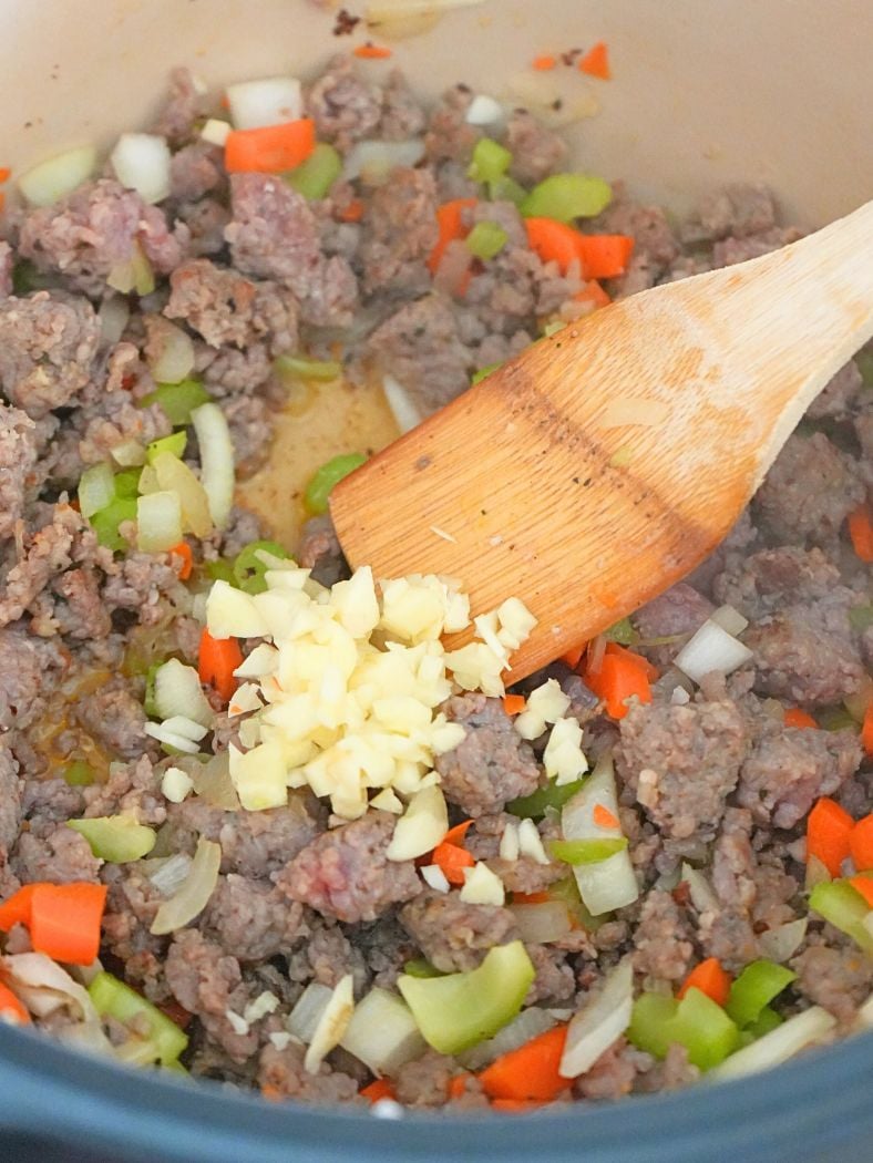 Minced garlic added to meat mixture in a Dutch oven