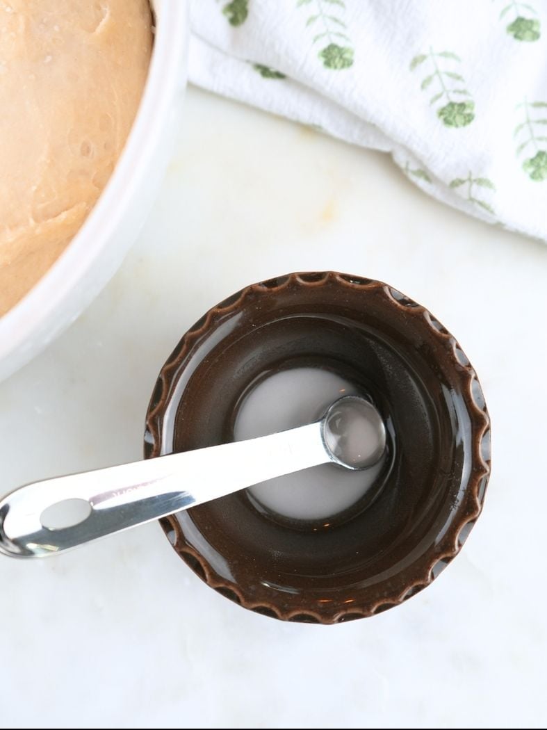 Baking soda and water mixed together in a small brown bowl, shown with a measuring spoon