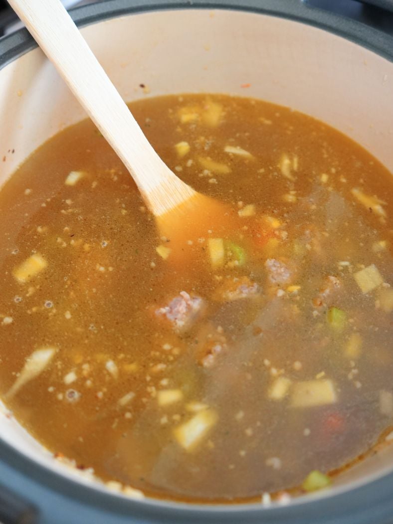 Broth poured into a large Dutch oven, shown with wood spatula