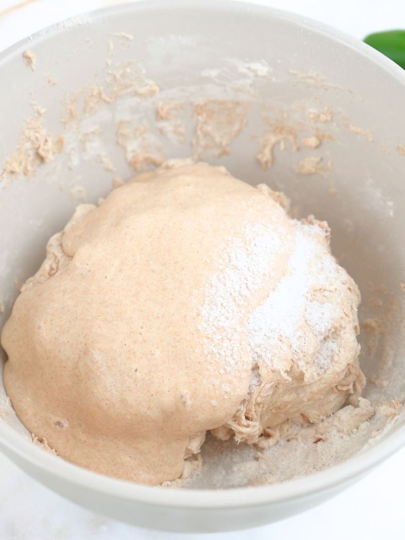 Sourdough starter and salt poured over dough in a mixing bowl