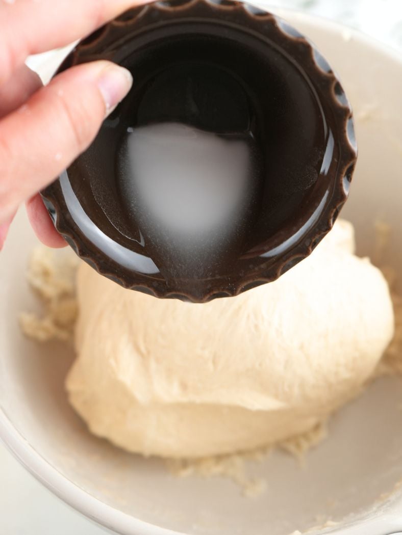A hand pouring baking soda and water mixture over dough
