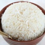 A close up of a bowl of white rice with a gold spoon