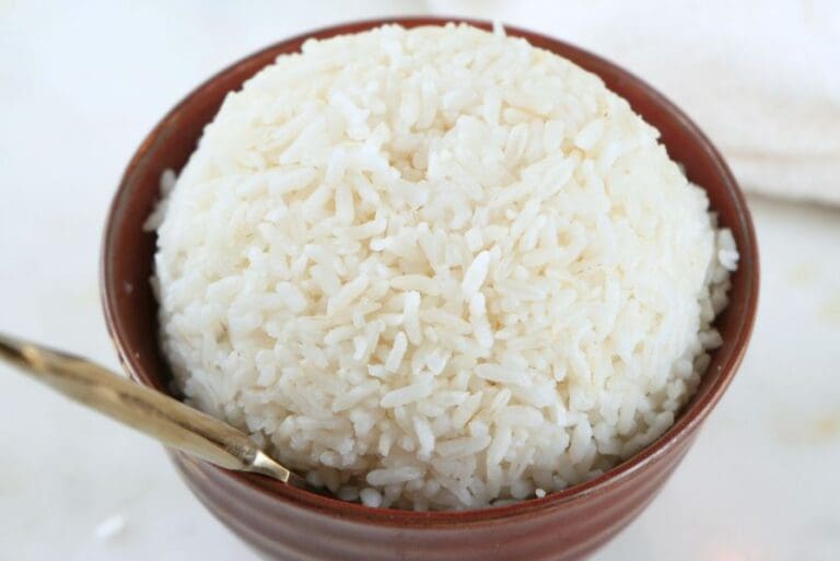 A close up of a bowl of white rice with a gold spoon